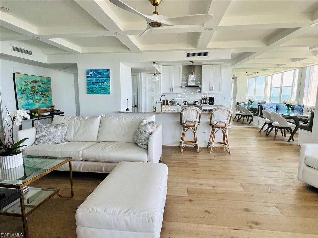 Open-concept living area with coffered ceilings, light wood-finish flooring, and white kitchen cabinetry