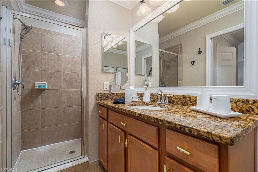 Bathroom with a glass-enclosed shower featuring large format tile, a vanity with a drop-in sink, and a stone countertop