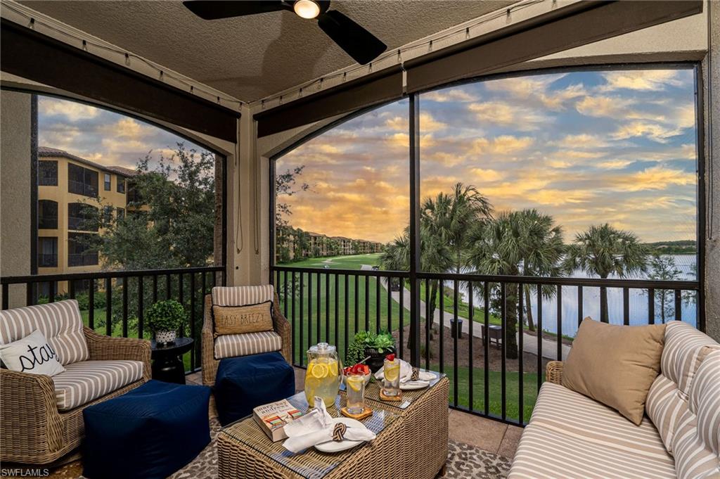 Screened balcony featuring a ceiling fan, a golf course, a body of water, and palm trees