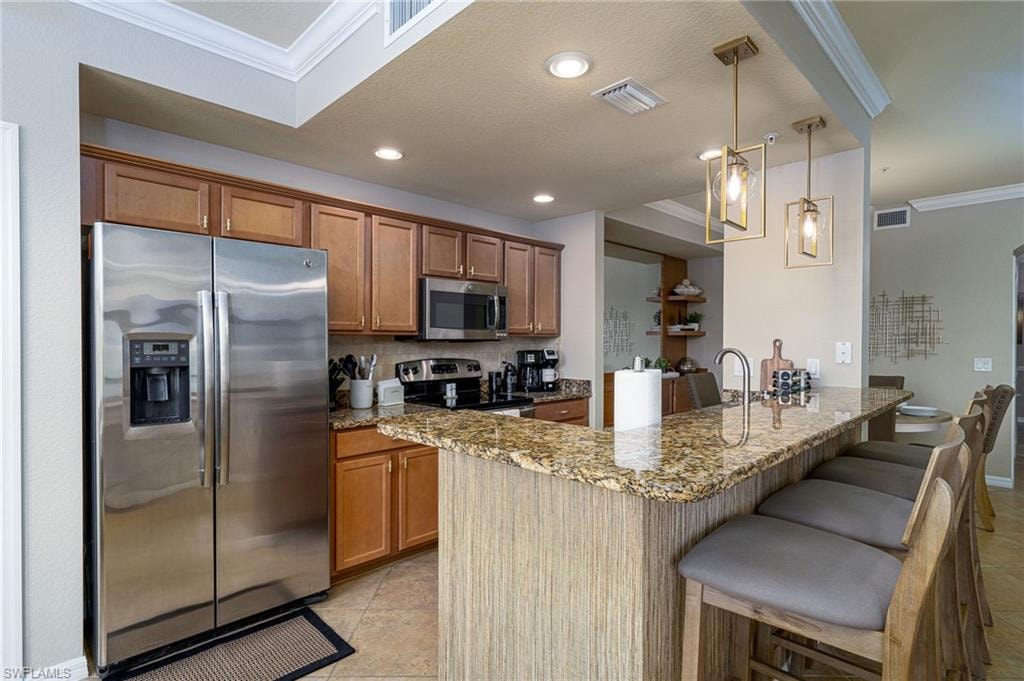 Kitchen featuring wood cabinetry, stainless steel appliances, and a breakfast bar with stone countertops