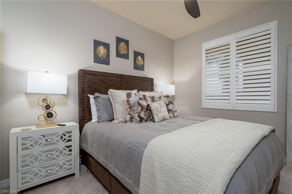 Bedroom featuring neutral wall paint, white plantation shutters, and a dark brown upholstered headboard with nailhead trim