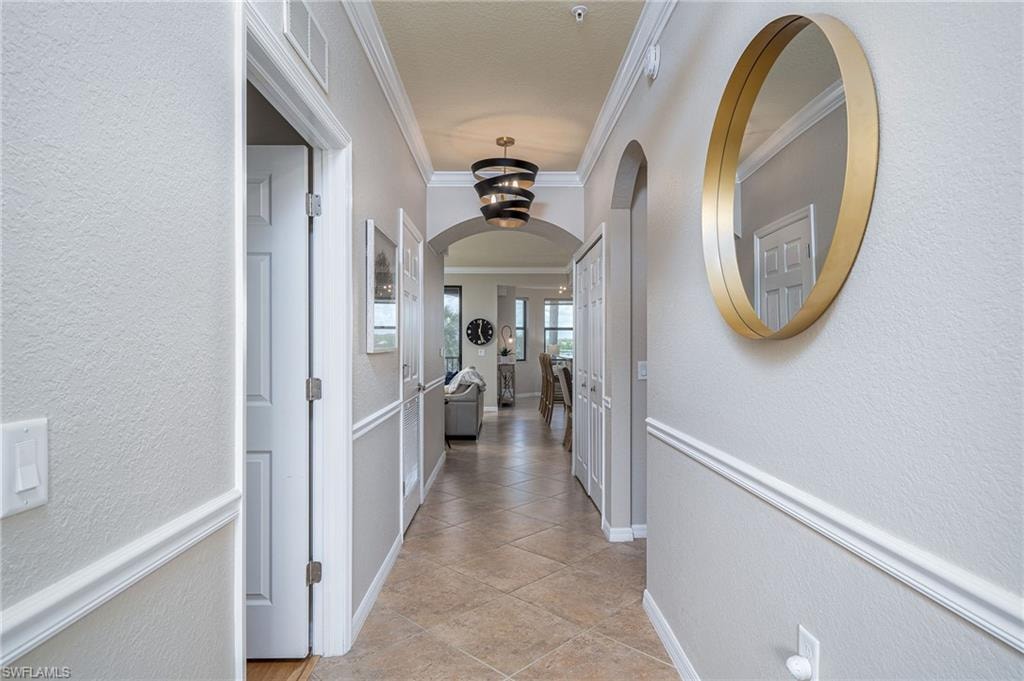 Hallway featuring tile flooring, wainscoting, crown molding, an arched entryway, and a contemporary chandelier