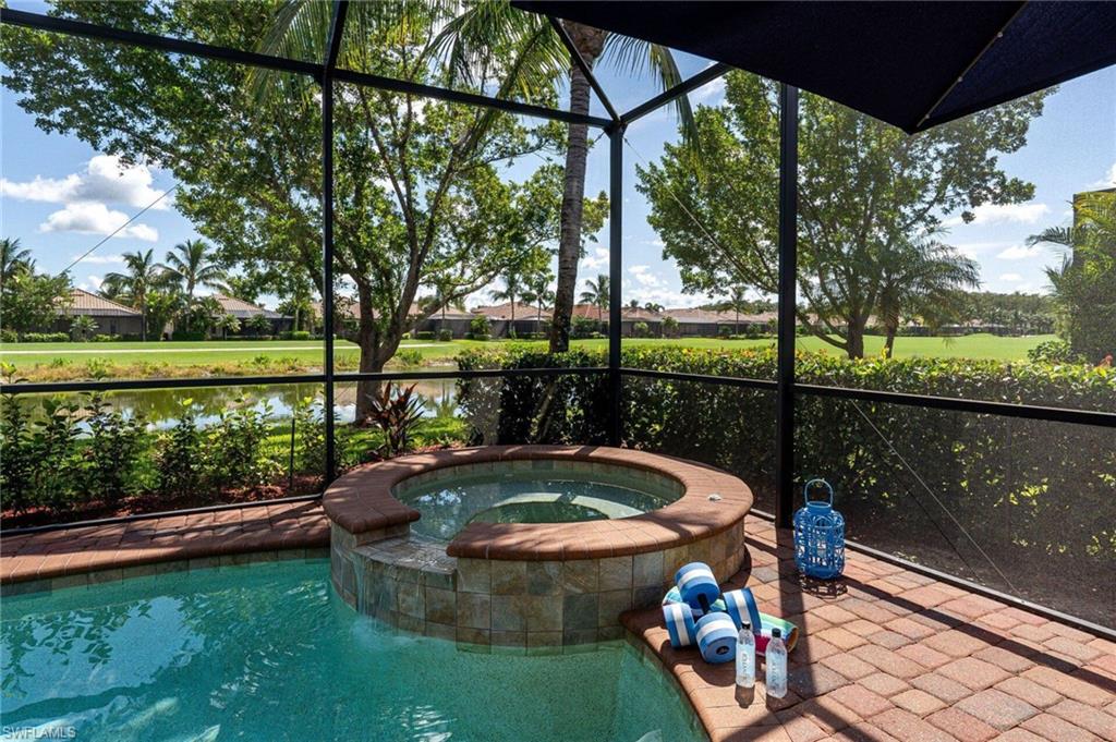 Screened outdoor area featuring a built-in spa with stone-tiled surround, a brick paver patio, and a swimming pool with a water feature