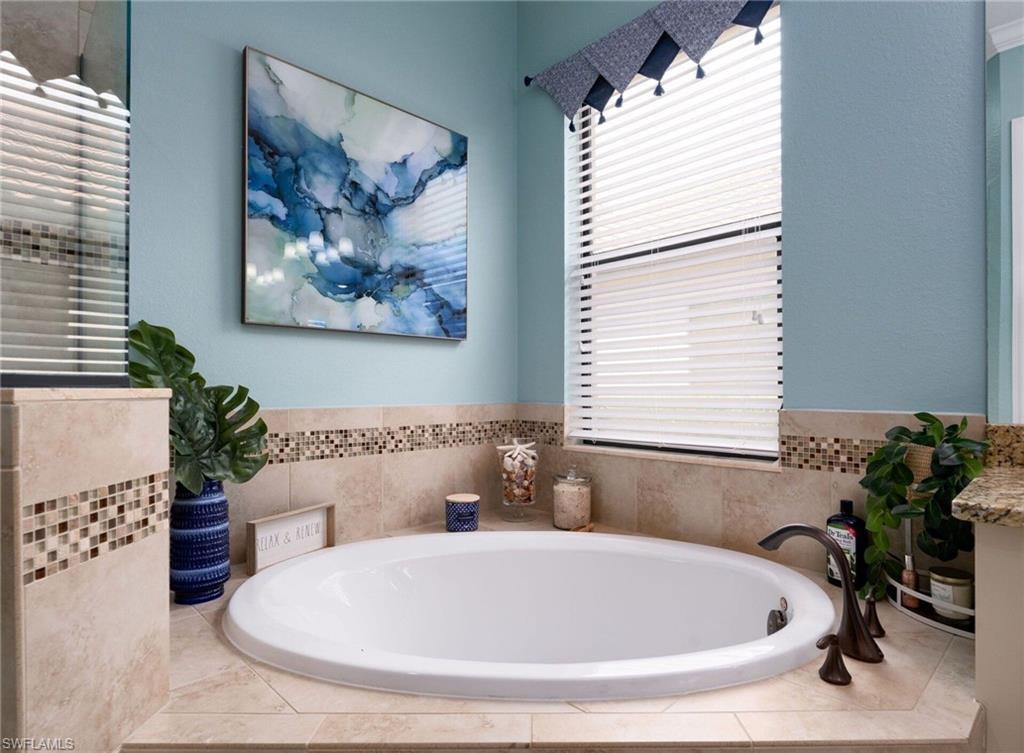 Soaking tub with bronze-finish fixtures, surrounded by neutral-toned tile and a decorative mosaic border