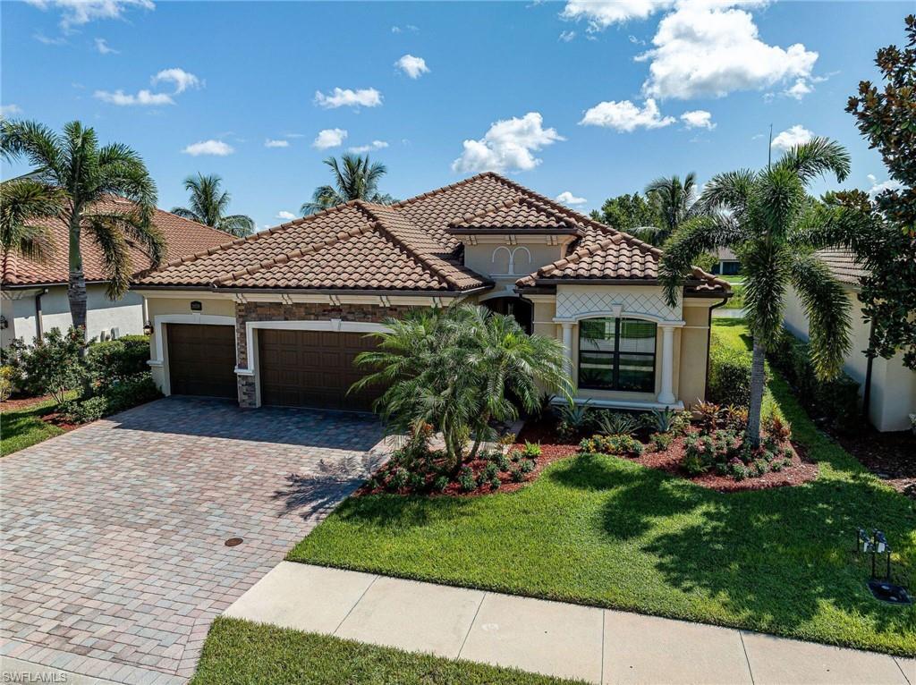 Mediterranean-style residence featuring a tile roof, two-car garage with paver driveway, and manicured landscaping