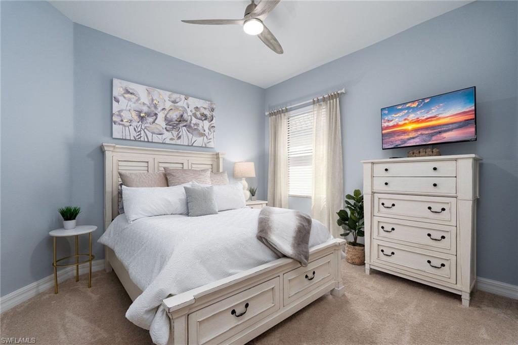 Spacious room featuring neutral carpeting, light blue wall paint, a ceiling fan with integrated lighting, and a window with blinds and drapes