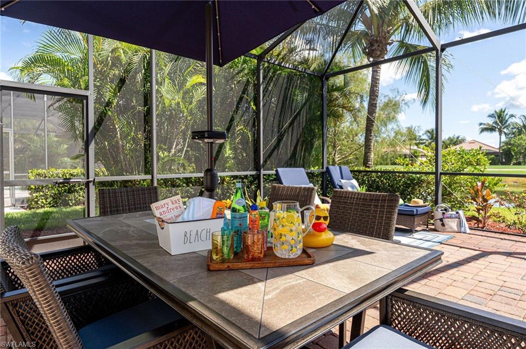 Screened lanai featuring a stone-top dining table, brick paver flooring, lush tropical landscaping, and water frontage
