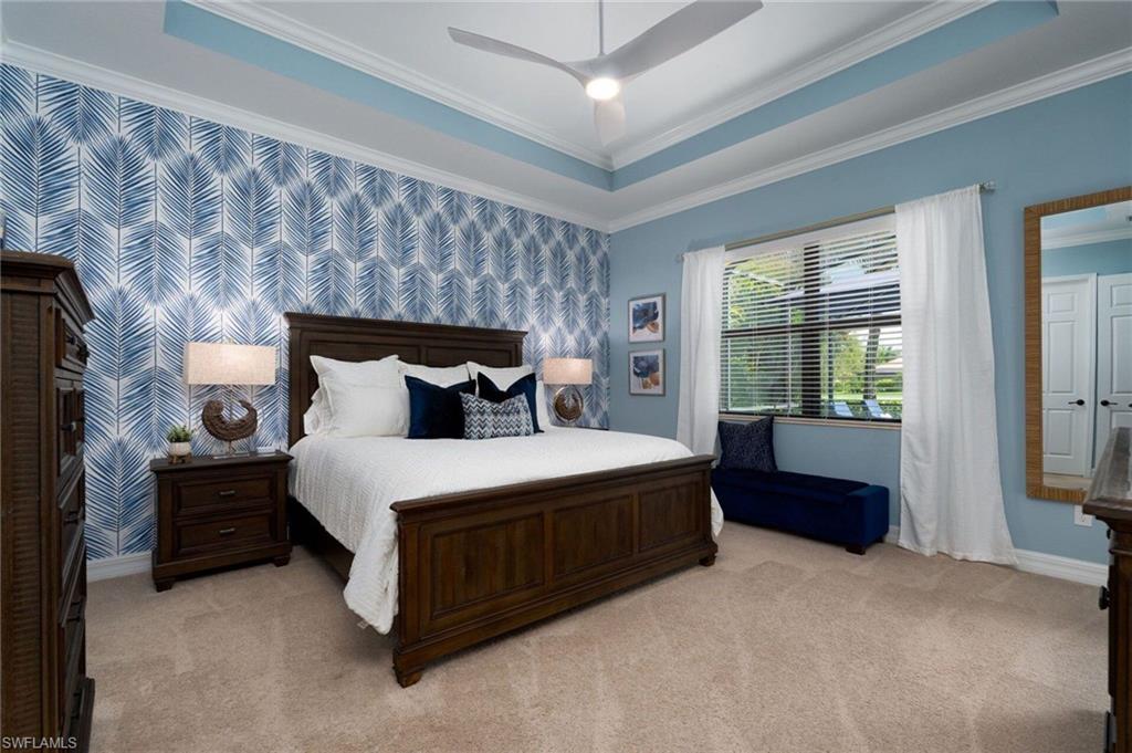 Bedroom featuring a tray ceiling with crown molding, patterned accent wall, light beige carpet flooring, and a large window with blinds and white drapes
