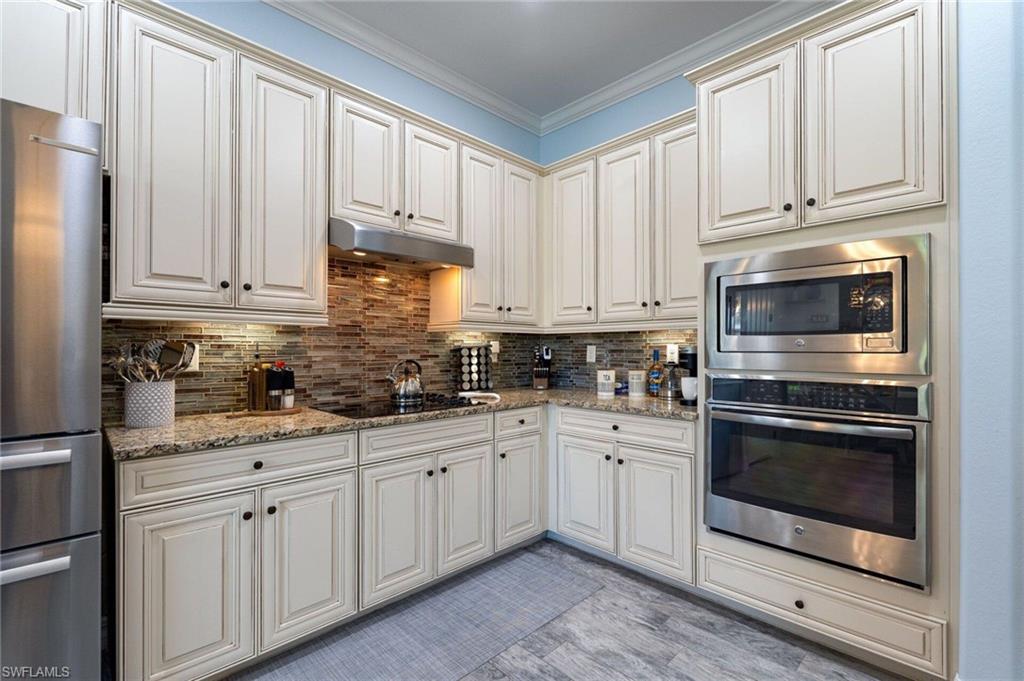 Kitchen featuring extensive white cabinetry, granite countertops, a built-in stainless steel microwave and oven, a stainless steel refrigerator, and a tiled backsplash