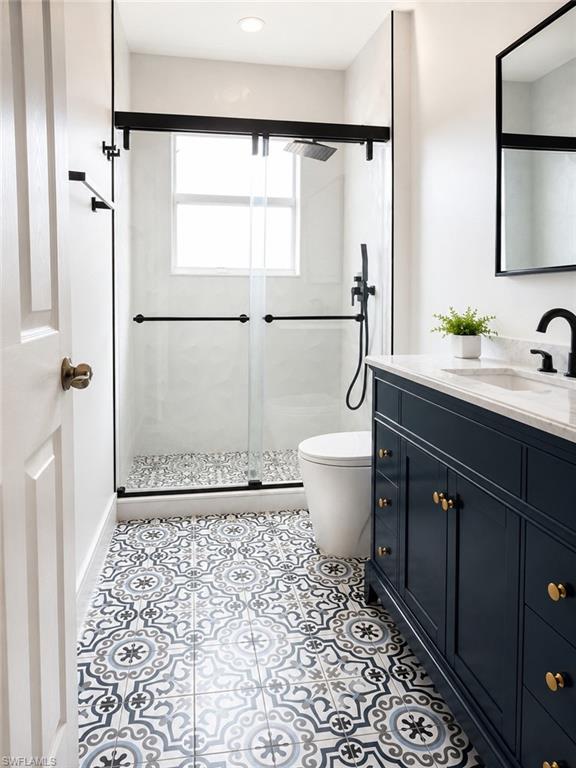 Bathroom on the second floor featuring decorative floor tiling, a dark blue vanity with brass hardware, a glass-enclosed shower with matte black fixtures, a window within the shower, and a frameless mirror