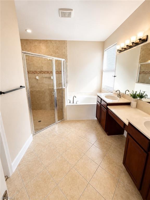 Spacious bathroom featuring diagonal tile flooring, a glass-enclosed shower with tiled walls and decorative banding, a separate soaking tub, and a dual vanity with dark wood cabinetry and light countertops