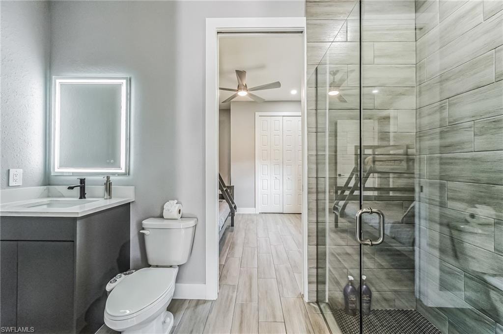 Bathroom featuring a frameless glass shower enclosure with horizontal tile surround, single vanity with a solid surface countertop, and an illuminated mirror