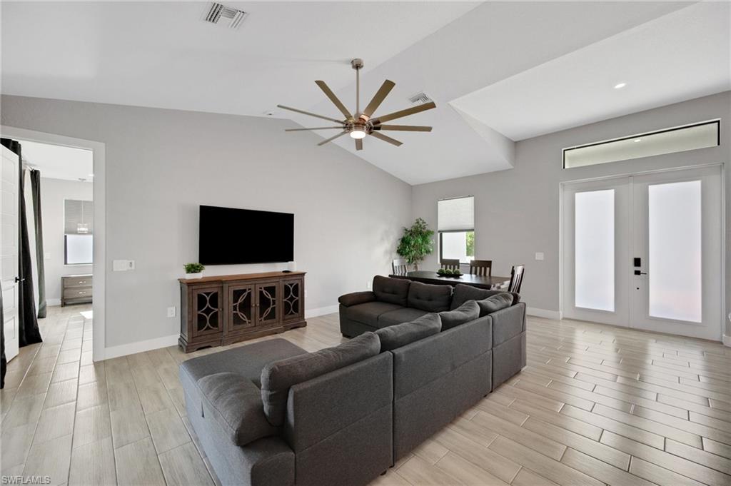 Open-concept living area with vaulted ceilings, large decorative ceiling fan, wood-finish tile flooring, double entry doors with transom window, and an integrated dining area