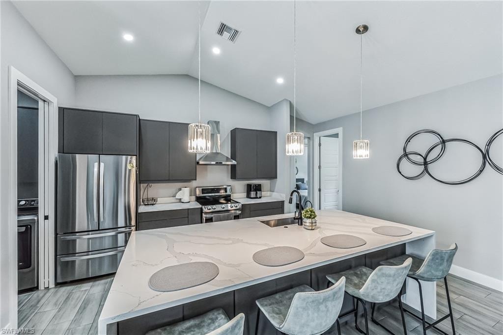 Kitchen featuring a waterfall island with an undermount sink, pendant lighting, stainless steel appliances, and wood-finish tile flooring