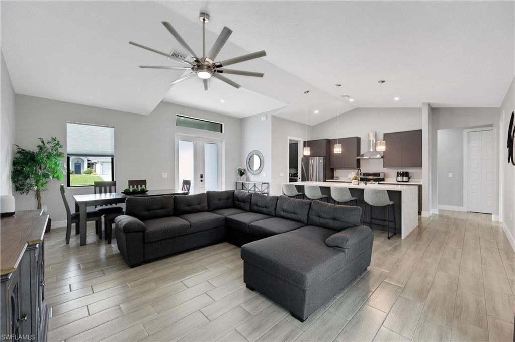 Spacious open-concept living area featuring wood-finish tile flooring, vaulted ceilings, and a modern ceiling fan