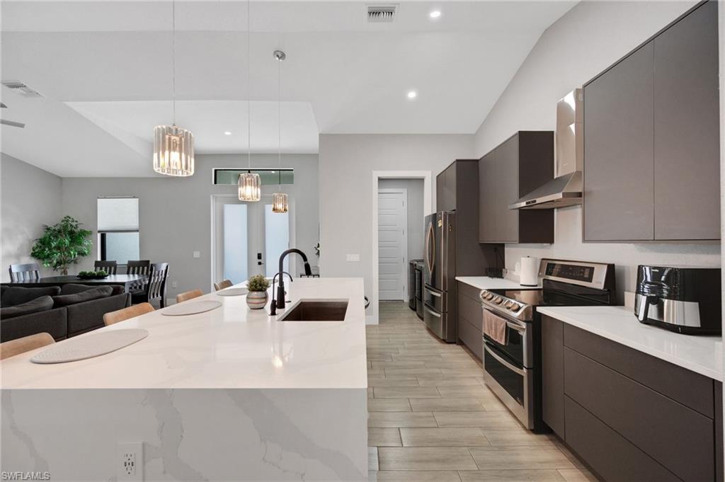 Modern kitchen featuring a waterfall-edge island with seating, stainless steel appliances, dark flat-panel cabinetry, and wood-finish flooring