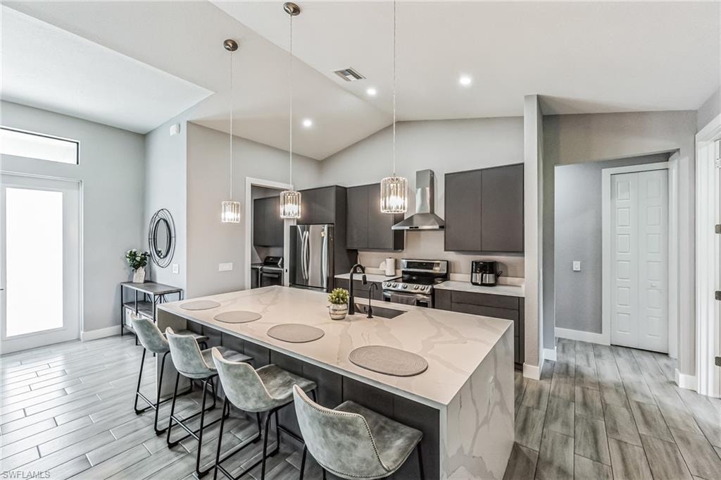 Gourmet kitchen featuring a large island with waterfall countertop, stainless steel appliances, dark gray cabinetry, and pendant lighting