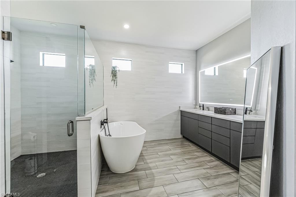 Modern bath featuring a frameless glass shower enclosure, a standalone soaking tub, and a dual vanity with a lighted mirror