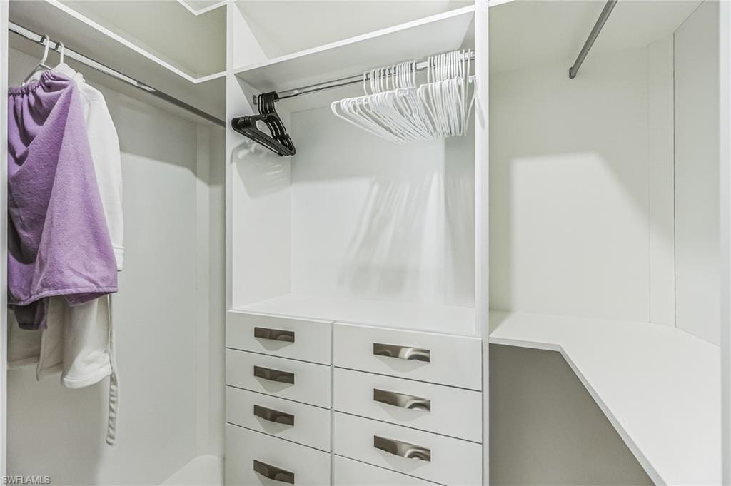 Custom white built-in closet system featuring multiple hanging rods, eight storage drawers with modern pulls, and integrated shelving