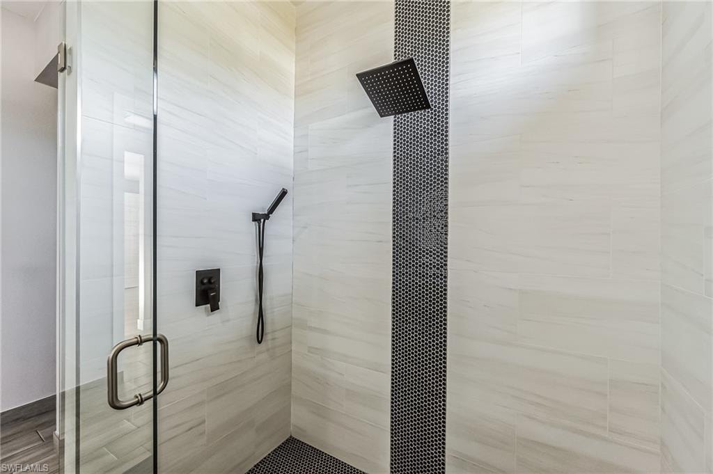 Walk-in shower featuring a frameless glass enclosure, white tile walls with subtle veining, and a vertical accent stripe of small black hexagonal tiles