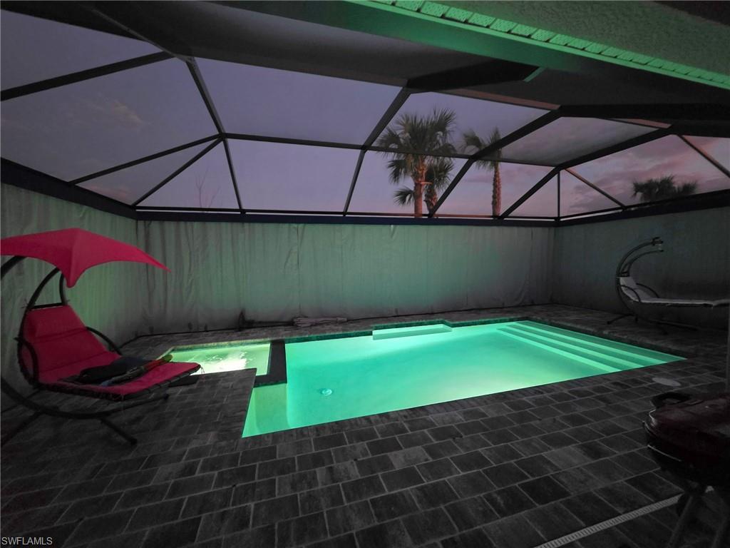 Screen-enclosed swimming pool area featuring a rectangular pool with integrated spa, paver decking, and surrounding privacy screening