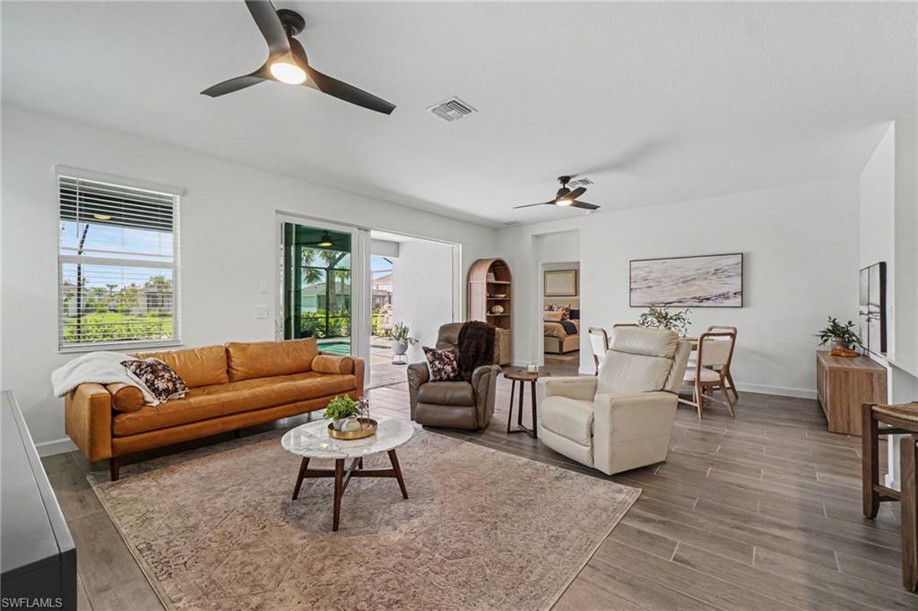 Spacious living area featuring wood-finish flooring, two modern ceiling fans with integrated lighting, and a window with horizontal blinds