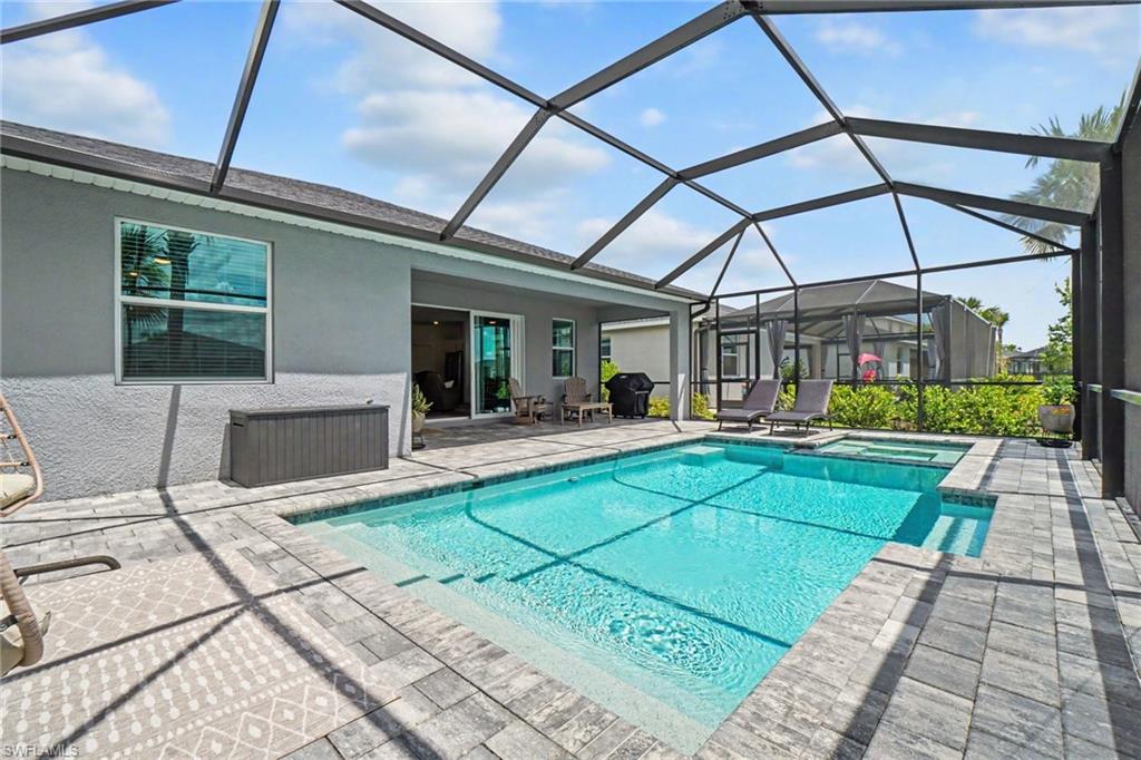 Screened-in outdoor living space featuring a swimming pool, integrated spa, and paver decking