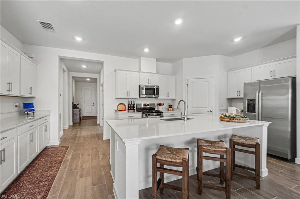 Modern kitchen featuring white cabinetry, light-toned countertops, stainless steel appliances, and wood-finish flooring