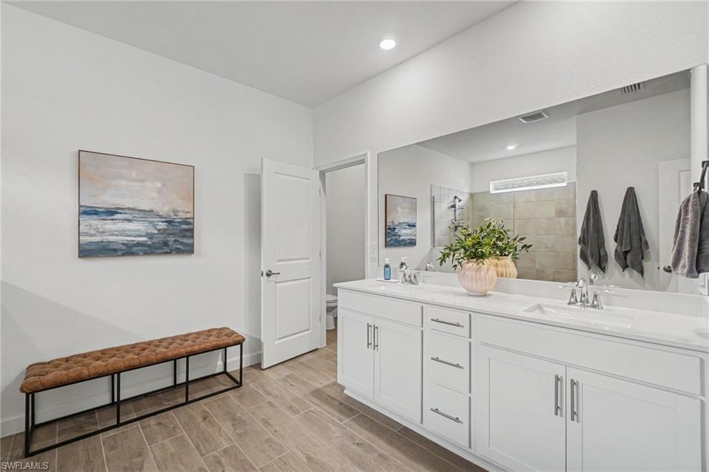 Spacious bathroom featuring a dual vanity with white cabinetry and integrated sinks, a large mirror, recessed lighting, and wood-finish tile flooring
