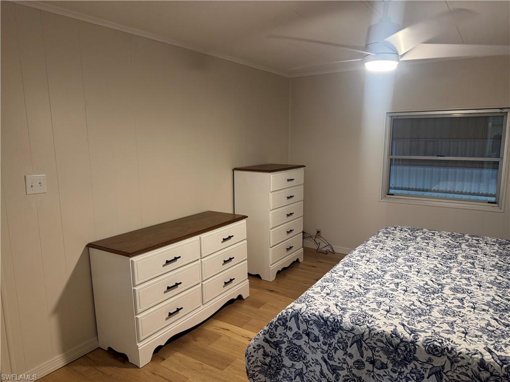 Room with light-toned wood-finish flooring, a white ceiling fan with integrated lighting, a window with horizontal blinds, and vertical paneling on the wall