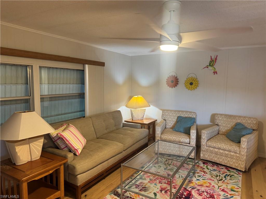 Living area featuring wood-finish flooring, a ceiling fan with integrated lighting, and multiple windows