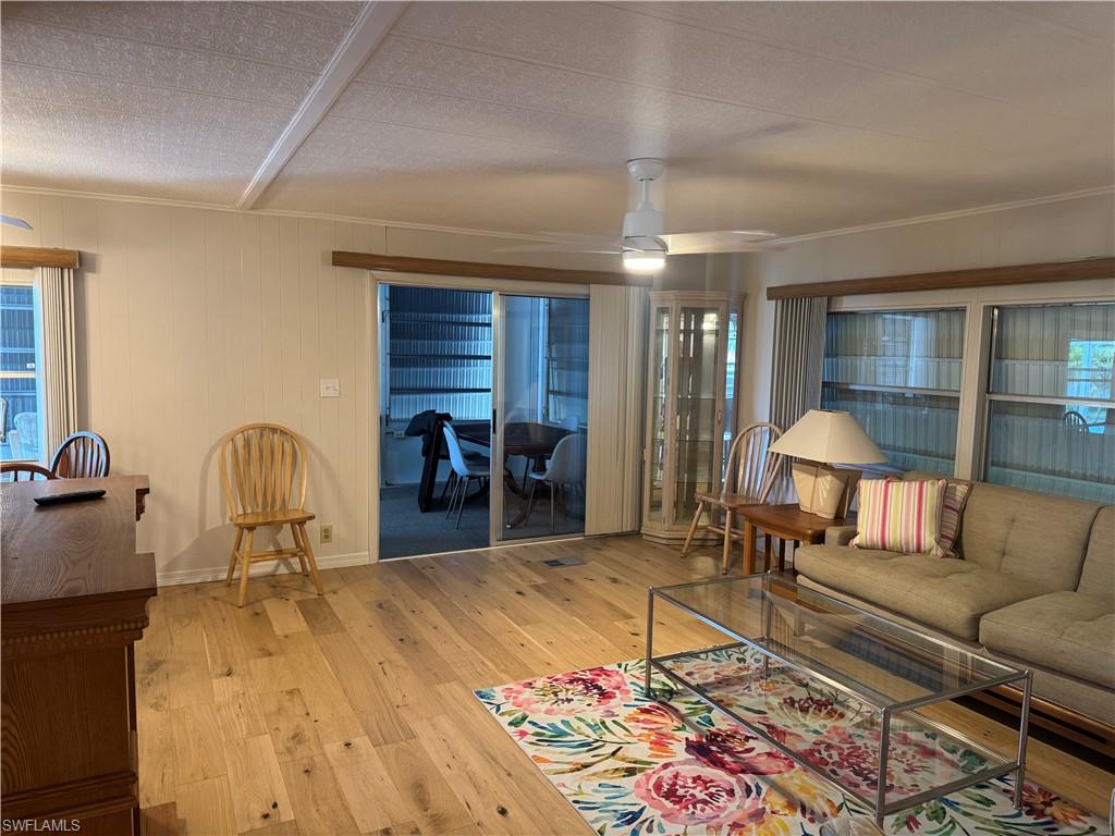 Expansive room featuring light wood-finish flooring, white paneled walls, and a ceiling fan with integrated lighting