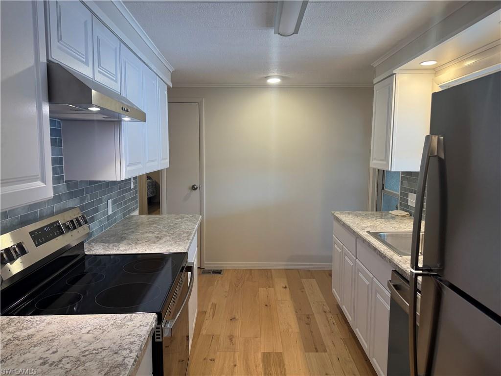 Galley kitchen featuring white cabinetry, light wood-finish flooring, a stainless steel electric range, a stainless steel refrigerator, and a blue subway tile backsplash
