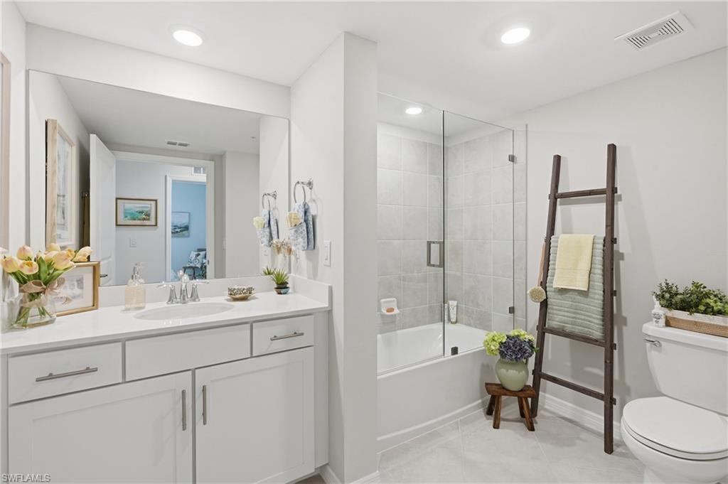 Modern bathroom featuring a single vanity with white cabinetry, a large frameless mirror, a shower-tub combination with a glass enclosure, and recessed lighting