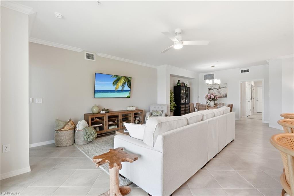 Spacious living area featuring light-toned tile flooring, crown molding, and a ceiling fan