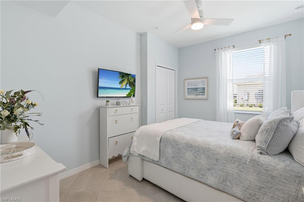 Bright bedroom featuring tiled flooring, a ceiling fan with integrated lighting, and a large window with white blinds and sheer curtains