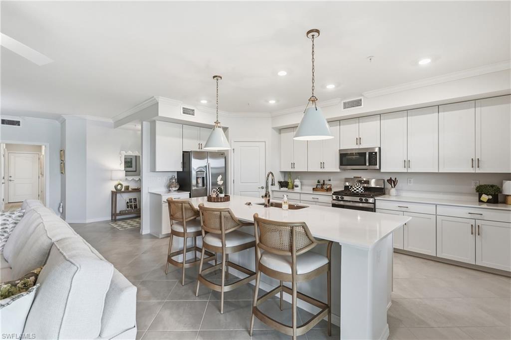 Kitchen featuring white shaker cabinetry, stainless steel appliances, a center island with pendant lighting, and light-toned tile flooring