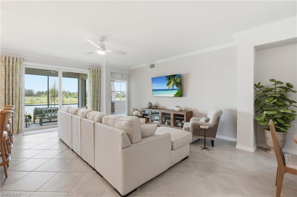 Spacious living area featuring large format tile flooring, crown molding, and a ceiling fan