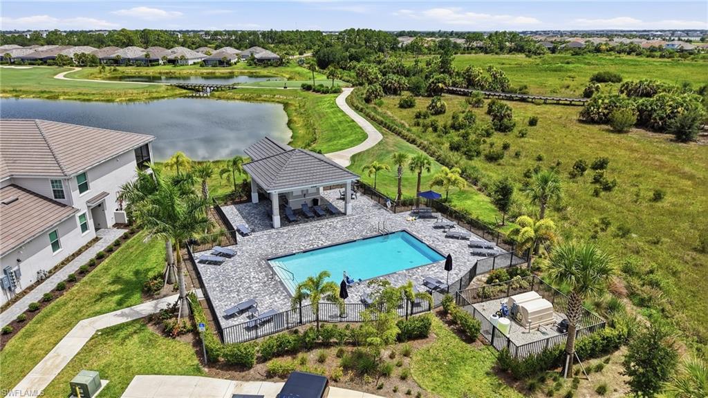 Community pool with a paver deck, covered lounge area, surrounding black fencing, and mature palm trees