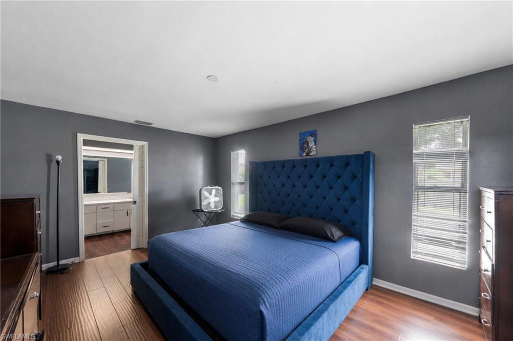 Bedroom featuring wood-finish flooring, two windows with blinds, and a doorway opening to a bathroom