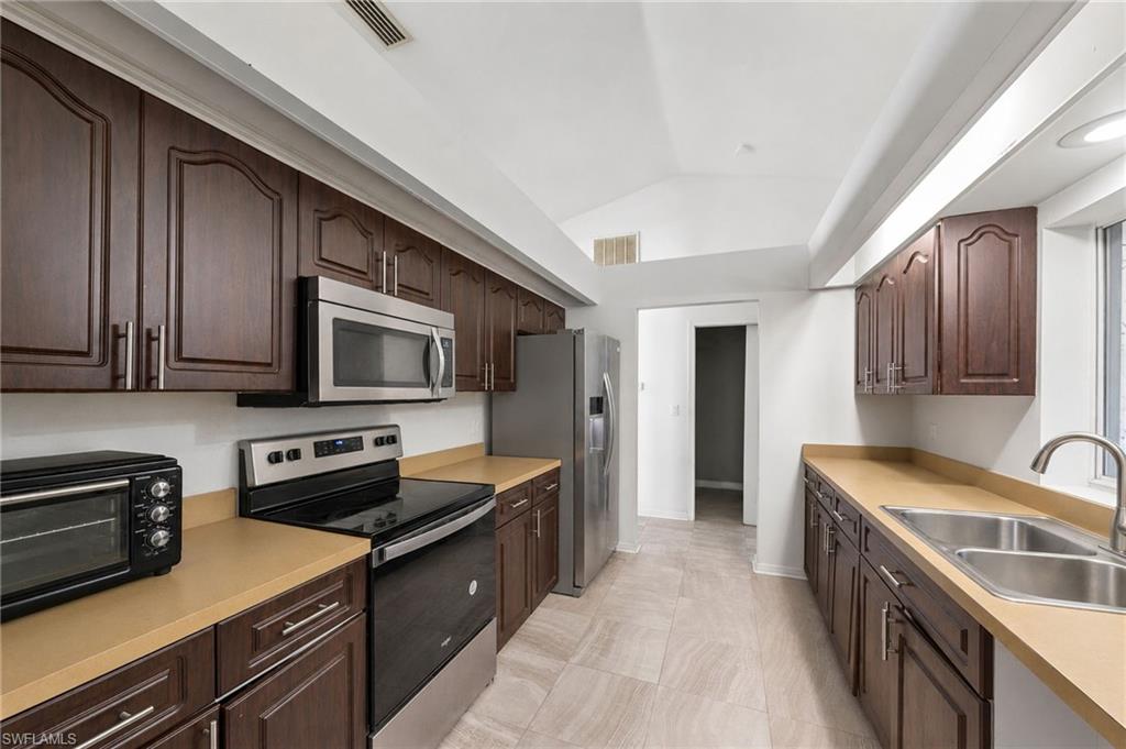 Galley kitchen featuring dark wood cabinetry, beige countertops, and stainless steel appliances