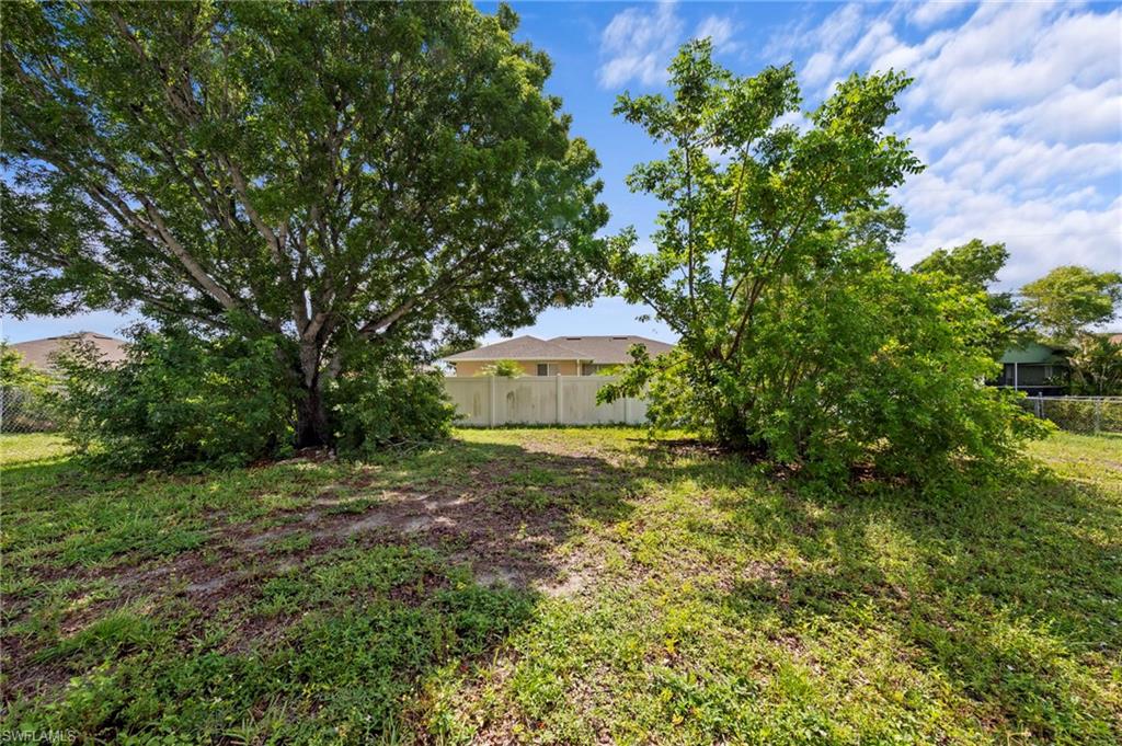 Expansive open lot featuring mature trees and a partial privacy fence