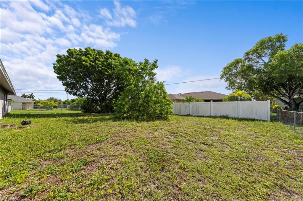 Expansive grassy yard featuring mature trees and a white privacy fence along one side