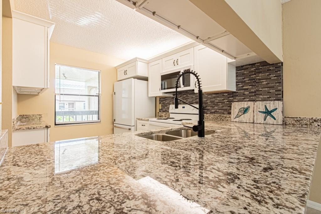 Spacious kitchen featuring granite countertops, white cabinetry, a dual basin stainless steel sink, a modern black pull-down faucet, and a decorative tile backsplash