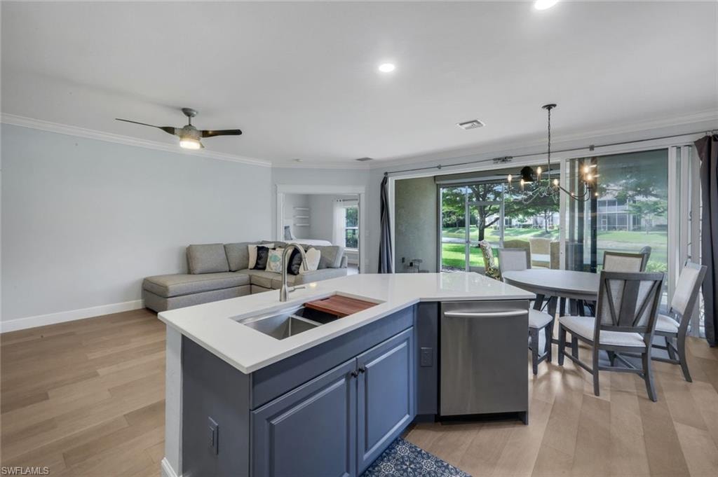 Open-concept living space featuring LVP flooring, a kitchen island with a double basin sink and stainless steel dishwasher, and a dining area with a chandelier