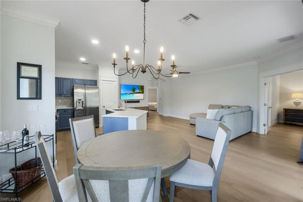 Open-concept living space featuring LVP flooring, a kitchen with blue cabinetry and stainless steel appliances, a central island with a white countertop, recessed lighting, and crown molding