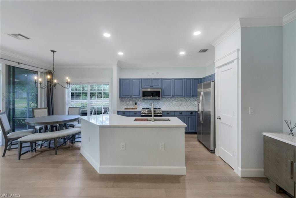 Open-concept kitchen and dining area featuring a white kitchen island with a built-in sink, blue cabinetry, stainless steel appliances, and LVP flooring
