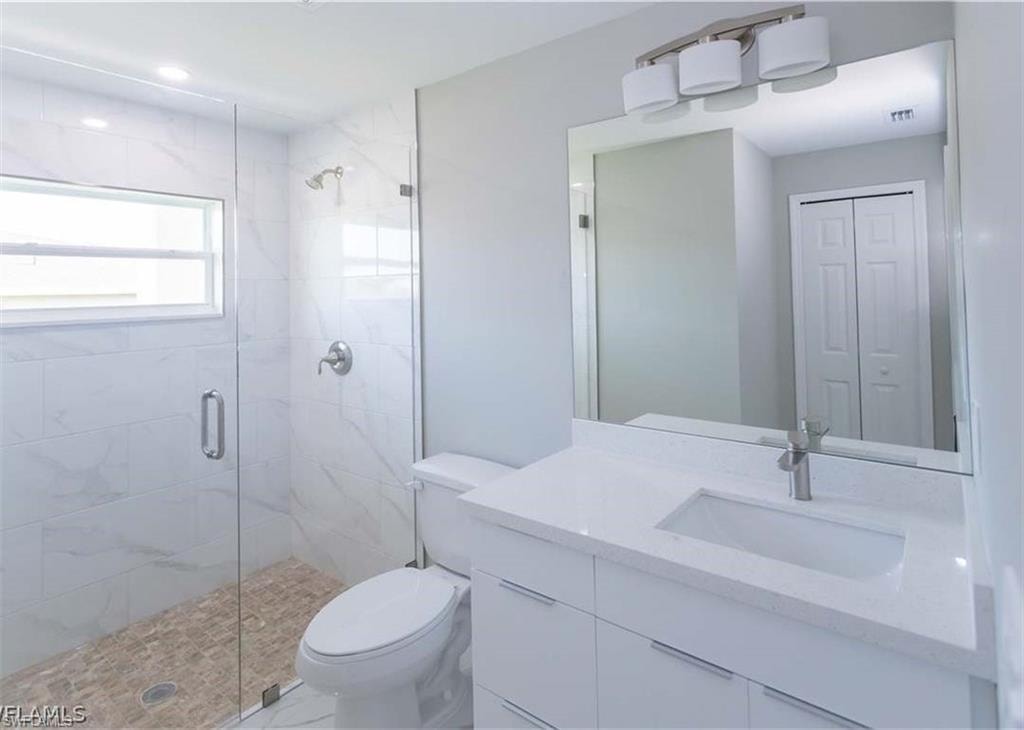 Contemporary bathroom featuring a frameless glass shower enclosure with marble-look tile walls and pebble flooring