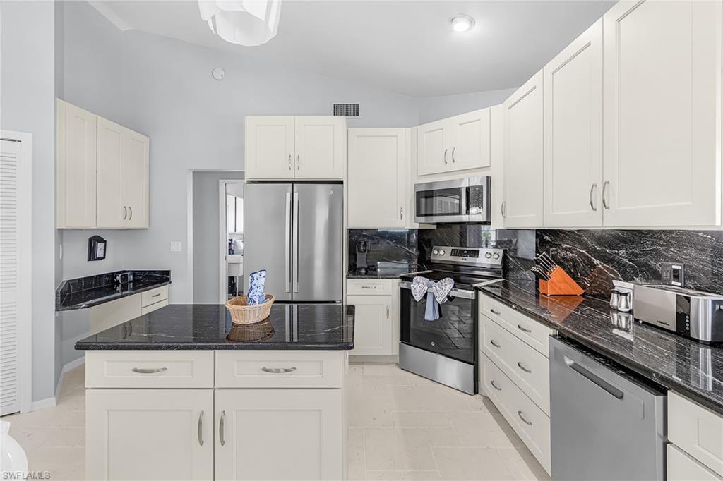 Kitchen with vaulted ceiling, appliances with stainless steel finishes, dark stone countertops, a kitchen island, and tasteful backsplash
