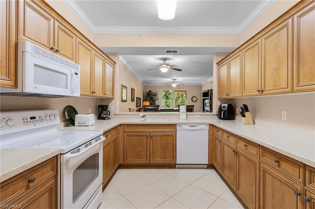 Kitchen featuring wood-finish cabinetry, light-toned countertops, and white appliances including a range, microwave, and dishwasher